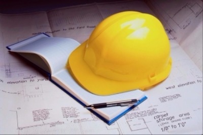 A yellow hardhat sitting on a notebook and plans.